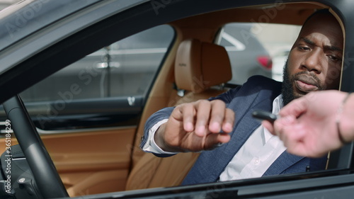 Closeup african man sitting front at car. Businessman taking key at vehicle © stockbusters