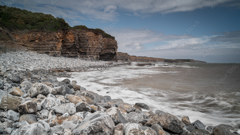 South Wales coastline, showing the water lapping against the rocky shore, flanked by high cliff.  The south Wales cliffs are composed partly of earliest Jurassic Sutton stone.