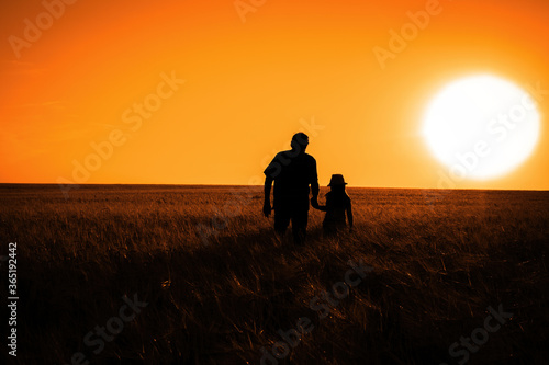 The silhouette of a man and a little girl in a field during sunset. Toned