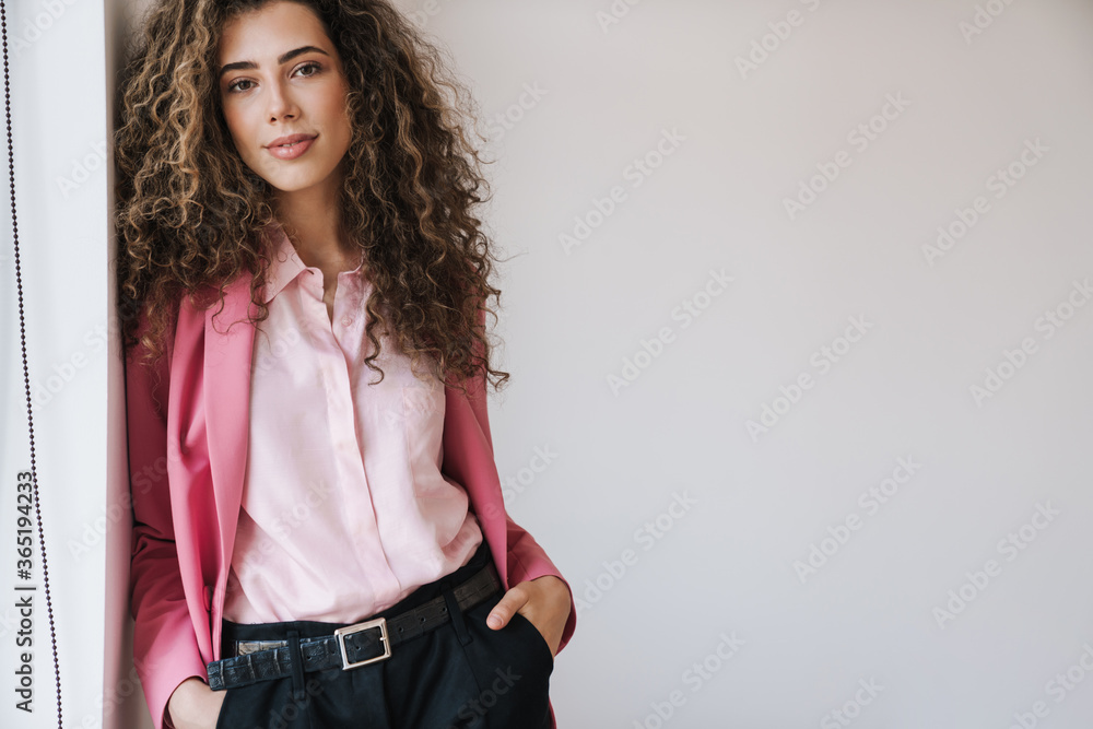 Photo of pleased beautiful woman posing on camera while leaning on wall