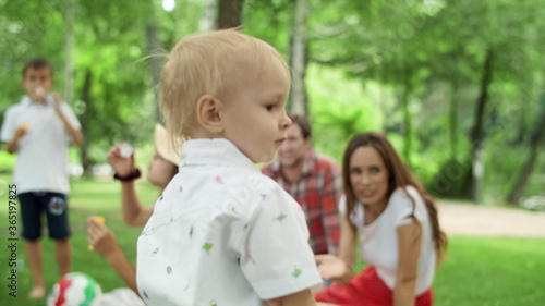 Toddler looking at camera with family. Children blowing soap bubbles in forest