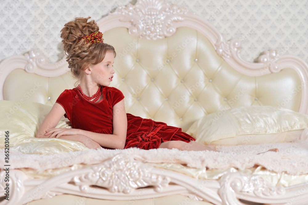 Cute little girl in red dress lying on bed