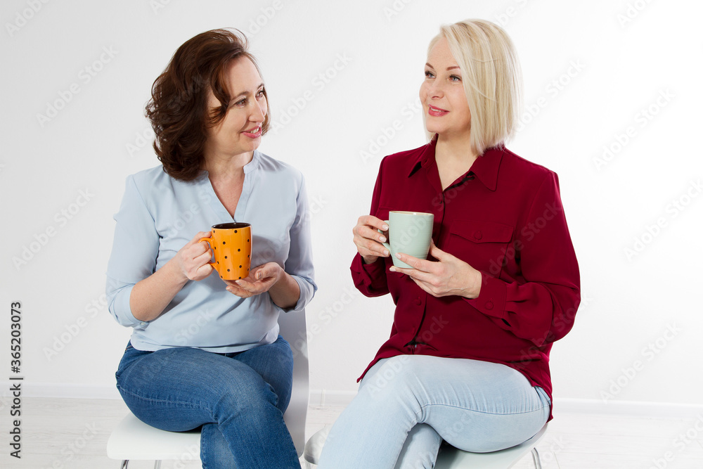 Two healthy and beautiful middle aged women drinking tea and talking isolated on white background. Woman support woman. Happy menopause concept. Two healthy and beautiful middle aged women drinking tea and talking isolated on white background. Woman support woman. Happy menopause concept.