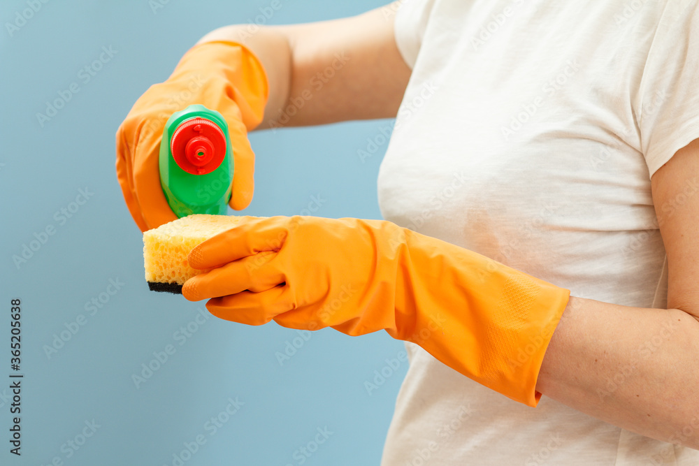 Woman holding a bottle of dishwashing liquid and a sponge on a blue background. Woman holding a bottle of dishwashing liquid and a sponge on a blue background.