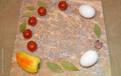 vegetables and two white eggs on a marble surface with free space: cherry tomatoes, bell peppers, garlic and bay leaves