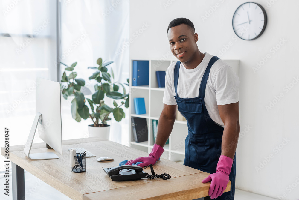 Smiling african american cleaner with rag standing near office table Smiling african american cleaner with rag standing near office table