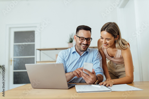 Smiling couple looking at smart phone at home office, portrait.