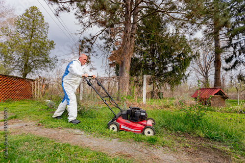 Farmer in protective clothing is mowing a lawn in a garden with a petrol lawn mower
