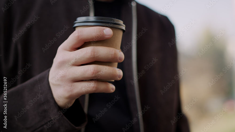 Man hand bringing takeaway coffee to lips. Guy hand holding paper cup outdoors. Man hand bringing takeaway coffee to lips. Guy hand holding paper cup outdoors.