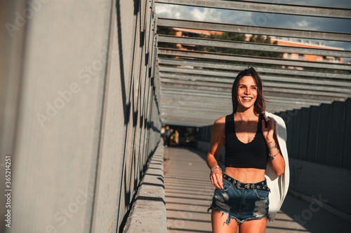 Scatto in prospettiva in una localit   metropolitana di una modella affascinante che cammina sorridente indossando un top nero e con in mano una giacca bianca