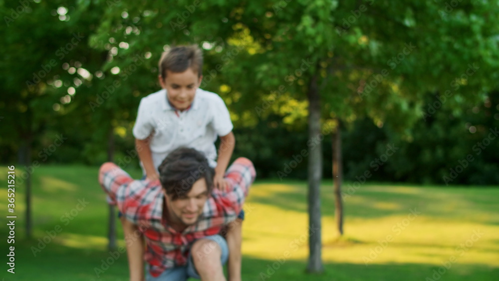Boy jumping on man back in field. Portrait of happy father carrying son on back Boy jumping on man back in field. Portrait of happy father carrying son on back