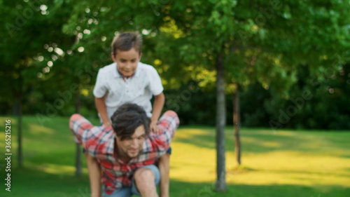 Boy jumping on man back in field. Portrait of happy father carrying son on back
