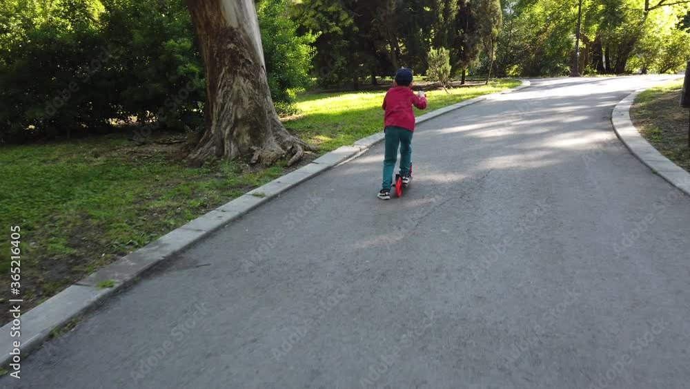 Happy little boy riding a scooter in the park. 4k video of boy riding kick scooter. Happy little boy riding a scooter in the park. 4k video of boy riding kick scooter.