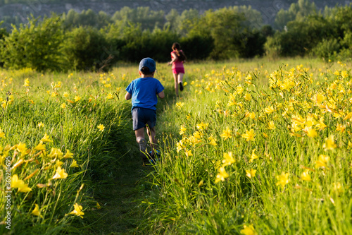 Cute  little boy and girl running in field with beautiful yellow flowers  summer. Happy childhood concept. © elena_siberia