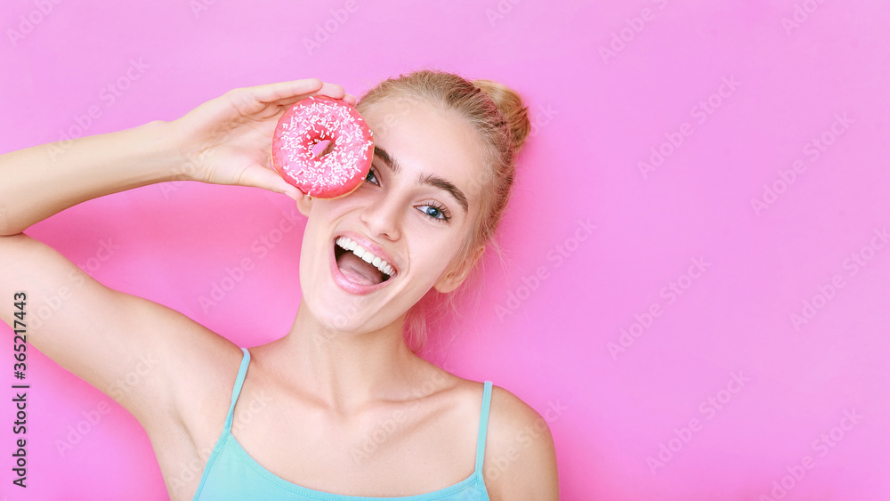 Girl with a donut on a pink isolated background. Face with a smile of a beautiful blonde girl who is holding a pink night lamp near her face. Copy space. Girl with a donut on a pink isolated background. Face with a smile of a beautiful blonde girl who is holding a pink night lamp near her face. Copy space.