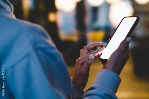 Women's hands hold mobile phone with big copy space touch screen outdoors with evening bokeh light of city on background. Close up view of female person using smartphone with blank advertise display