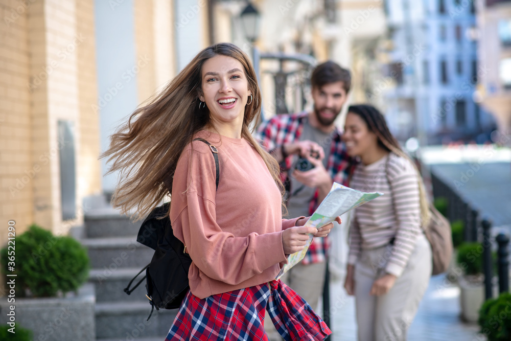 Happy long-haired girl with backpack and map in her hands.