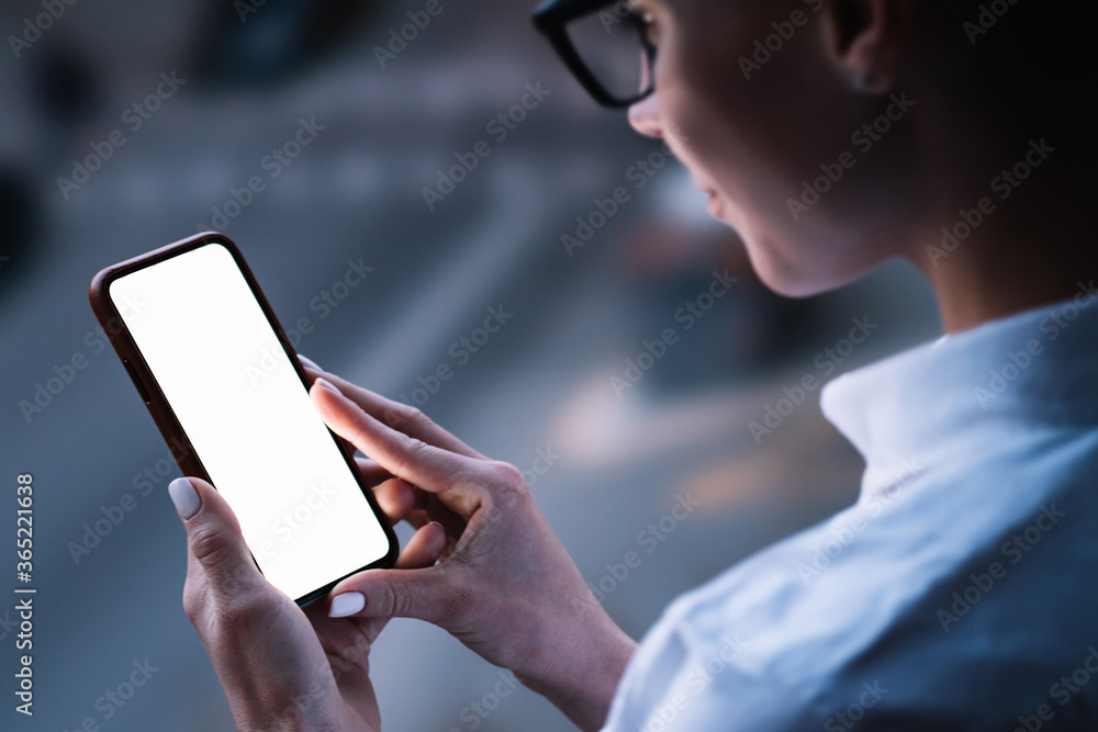 Woman's hands holding mobile phone with lighted big copy space touch screen outdoors with evening bokeh light of city. Close up view of female person using smartphone app for online shopping