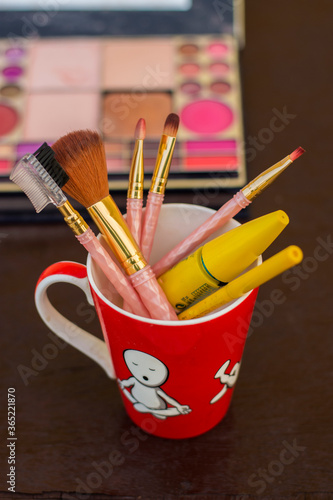 different types of makeup brushes with muskcara and kajol pencil in a red mug selective focus photo