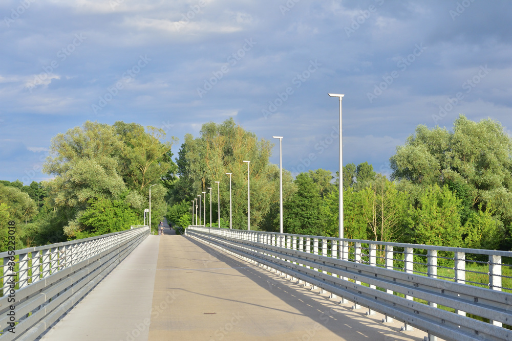 The bridge and lamps against the backdrop of trees and a cloudy sky.