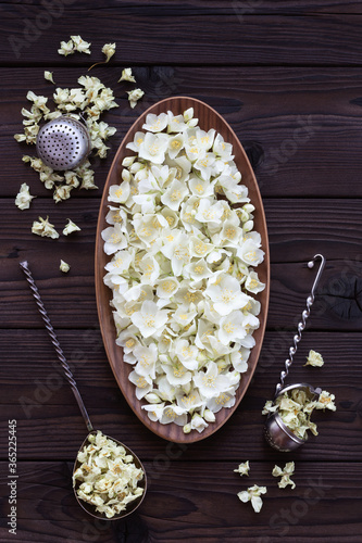 Fresh and dried jasmine flowers on a dark wooden table. Harvesting flowers for flavoring tea. Jasmine flowers in an oval wooden dish and retro tea strainers.