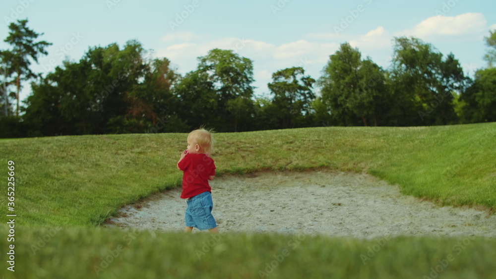 Boy walking in green field. Cheerful child holding ball in hands outdoors Boy walking in green field. Cheerful child holding ball in hands outdoors