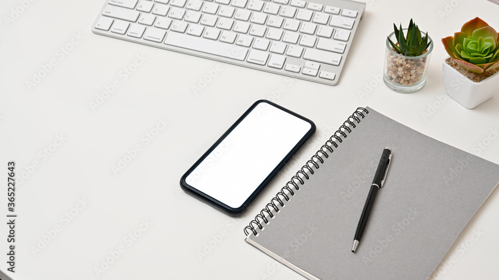 Cropped shot view of modern home office workspace with smartphone and notebook on white table. Cropped shot view of modern home office workspace with smartphone and notebook on white table.