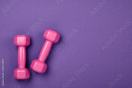 Fitness concept. Weight loss. Pink dumbbells isolated on purple yoga mat. With copy space for text
