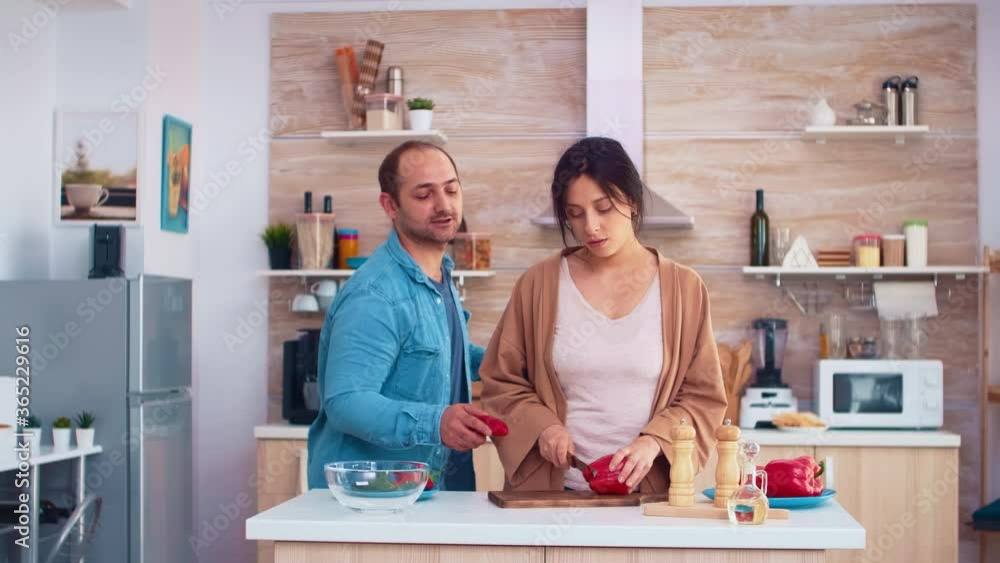 Man singing on red pepper in kitchen making wife smile. Girlfriend preparing salad. Cooking preparing healthy organic food happy together lifestyle. Cheerful meal in family with vegetables
