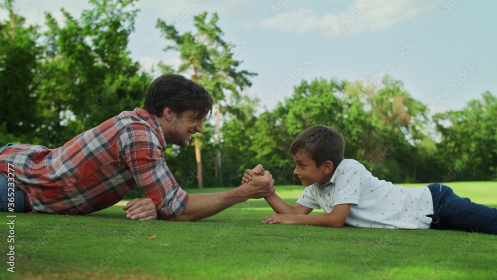 Boy and man armwrestling on grass. Father and son practising arm wrestling Boy and man armwrestling on grass. Father and son practising arm wrestling