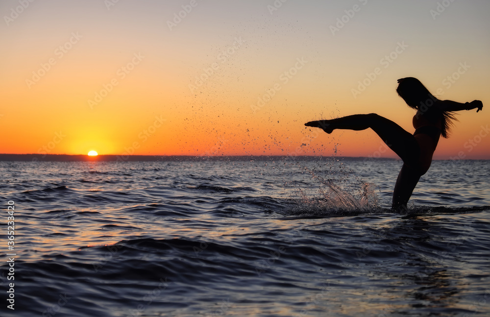 The girl swims in the sea, splashes in the water at sunset. Relaxation and happy pastime. Summer vacations. Water kick.