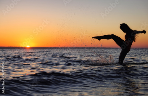 The girl swims in the sea, splashes in the water at sunset. Relaxation and happy pastime. Summer vacations. Water kick.