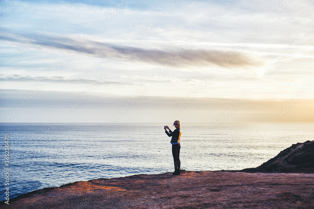 Silhouette of female taking photo of beautiful sea landscape on mobile phone camera while standing on mountain rock, young woman shoots video of an amazing scenery view of calm ocean on cell telephone Silhouette of female taking photo of beautiful sea landscape on mobile phone camera while standing on mountain rock, young woman shoots video of an amazing scenery view of calm ocean on cell telephone