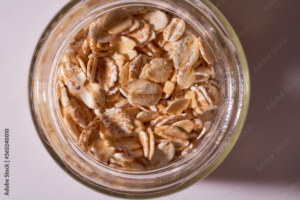 Oat flakes lie in a snitch jar on a white background. Close-up. With copy space.