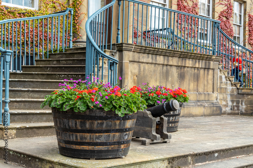 Wooden half barrel planters with red and purple flowers by the elevated entrance of a large mansion house. photo