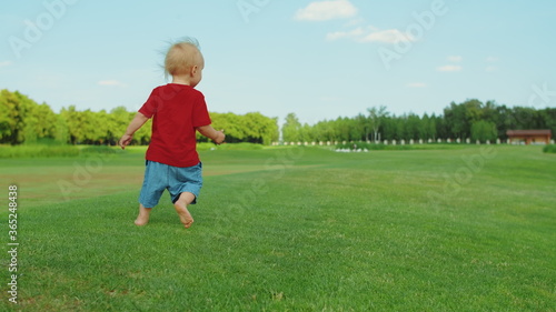 Small boy running in field. Blonde kid having fun in green meadow