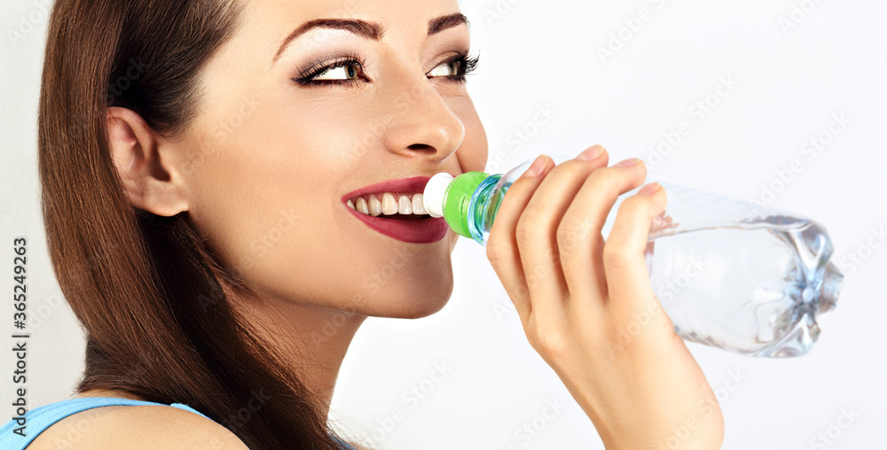 Beautiful happy toothy smiling fitness woman drinking water from the bottle holong in the hand. Healthy face skin. Closeup Beautiful happy toothy smiling fitness woman drinking water from the bottle holong in the hand. Healthy face skin. Closeup