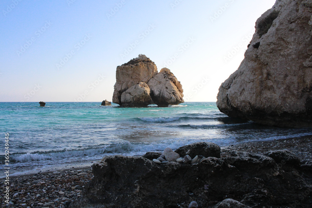 Stones on the beach of Aphrodite and the legendary Aphrodite's Rock on the background of blue cloudless sky. Cyprus.