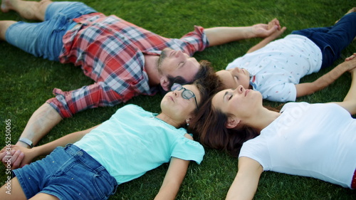 Family lying on green grass in circle. Cute kids and parents relaxing in field