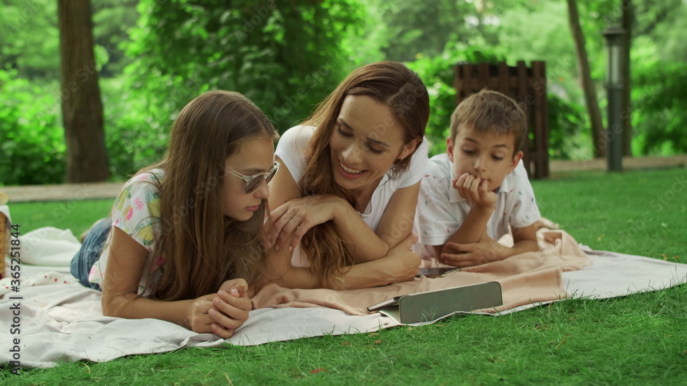 Mother with children looking at tablet screen in park. Family using pad outside