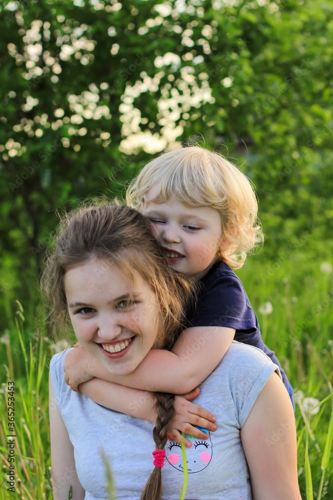 Cute teenager girl and little blonde boy playing and laughing on a green meadow. Sister and brother, siblings. Summertime, family concept. Cute teenager girl and little blonde boy playing and laughing on a green meadow. Sister and brother, siblings. Summertime, family concept.