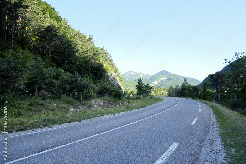 Mountain road in French Alpes on a sunny summer morning, beautiful natural landscape for travel design, empty rural road with picturesque scenery