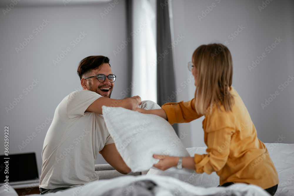 Obraz premium Young couple fighting pillows on the bed. Happy couple having fun at home. 