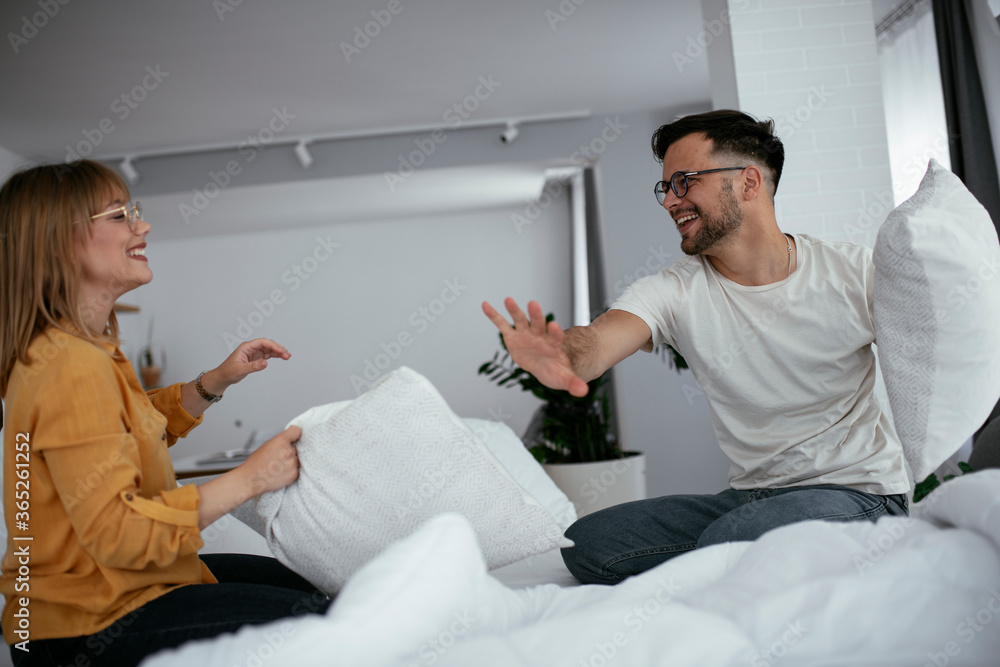 Obraz premium Young couple fighting pillows on the bed. Happy couple having fun at home. 