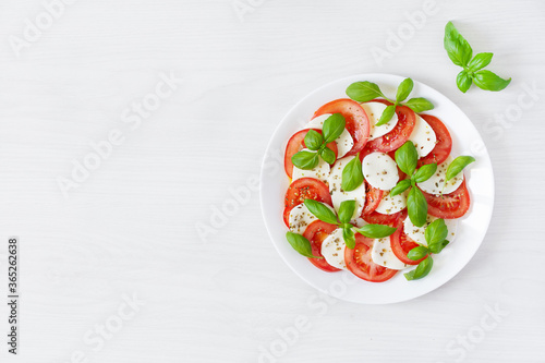 Caprese salad with mozzarela, tomatoes, fresh olive oil and basil on white background top view.