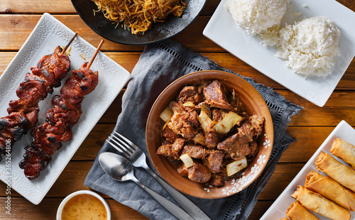 pork adobo meal with filipino foods such as lumpia, pancit noodles, and rice photo