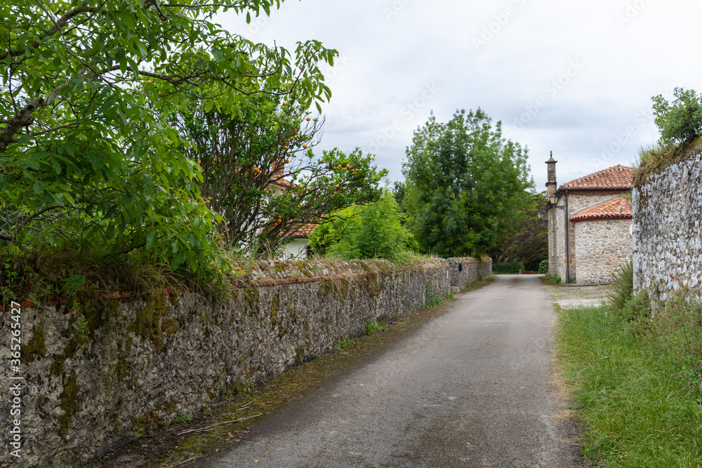 Rural road view with trees and stone wall, with a small church in the background, in Cantabria, Spain, horizontal
