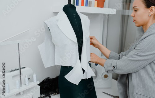 Young woman tailor is arranging a future shirt on a mannequin in her mini workshop. photo