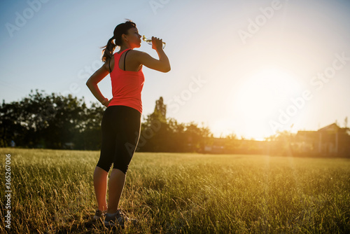 Woman is drinking water on a grass after making sport and running on a sunset © Med Photo Studio