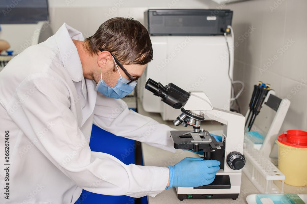 In the hospital laboratories working process, a young man doctor is looking in the medical microscope In the hospital laboratories working process, a young man doctor is looking in the medical microscope